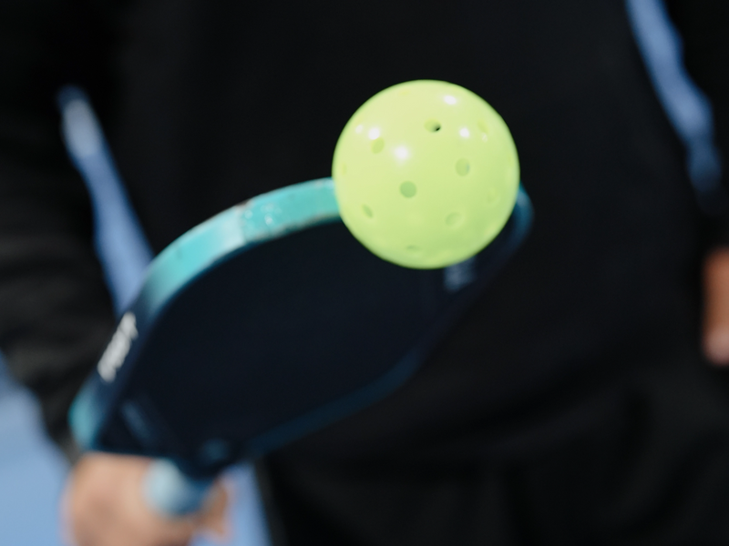 Pro pickleball player Ryan Sherry demonstrating Pickle Putty with a ball attached to his paddle, highlighting its easy ball pickup feature