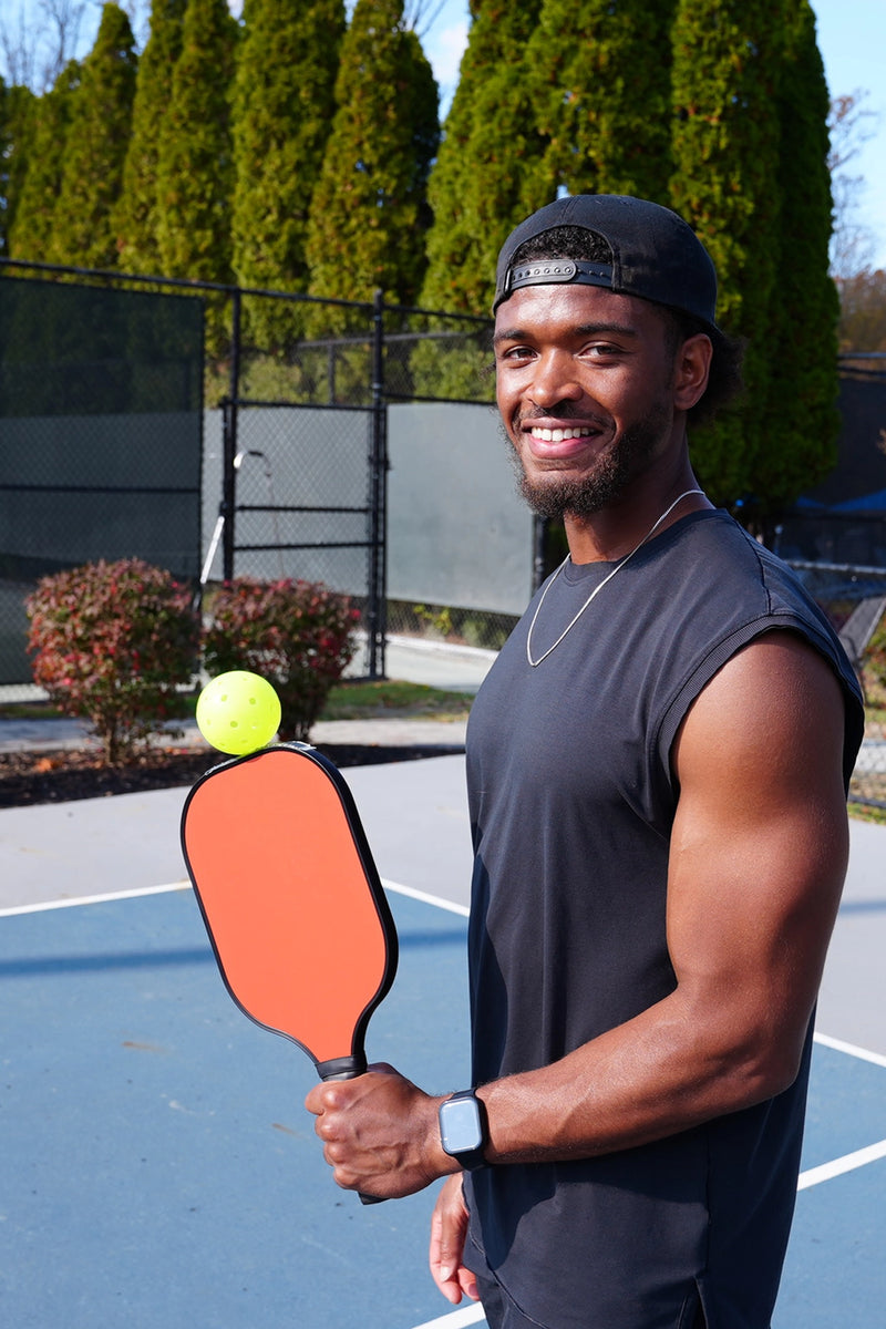 A smiling pickleball player holding a paddle with Pickle Putty attached, effortlessly picking up a pickleball without bending.