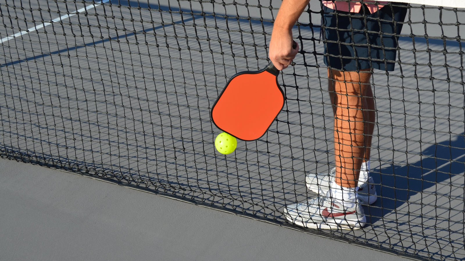 A pickleball player using Pickle Putty to easily retrieve a ball from the net with a paddle, making ball pickup effortless and convenient.